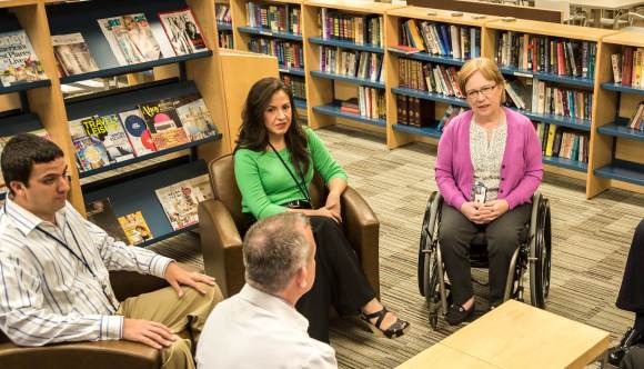 A group of professionals and Veterans engage in a discussion in a library setting. The group, seated in a circle of chairs, represents a mental health or support session at VA, emphasizing collaboration and care for Veterans.